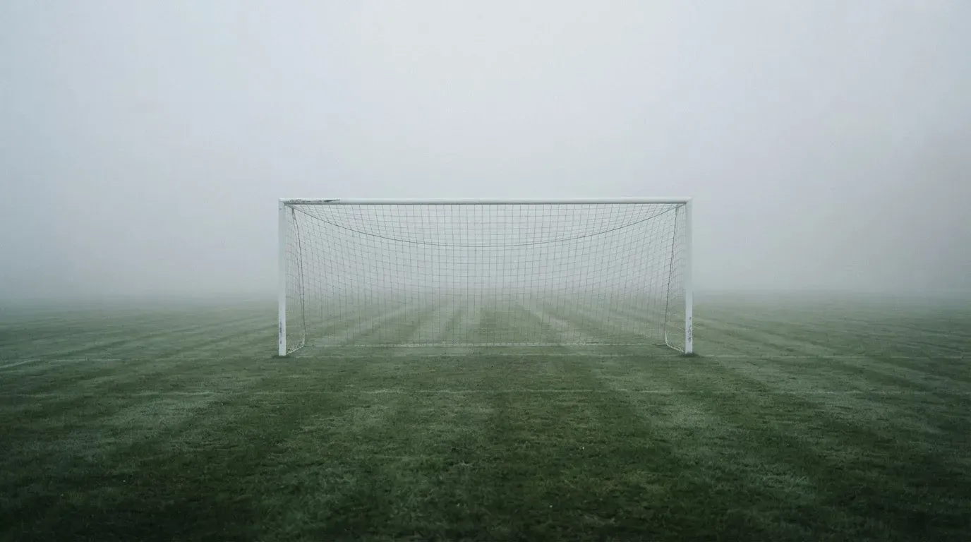 Eine Torlinie mit Netz steht am frühen Morgen im dichten Nebel auf einem Rasenplatz, die Umrisse der Pfosten verschwimmen.