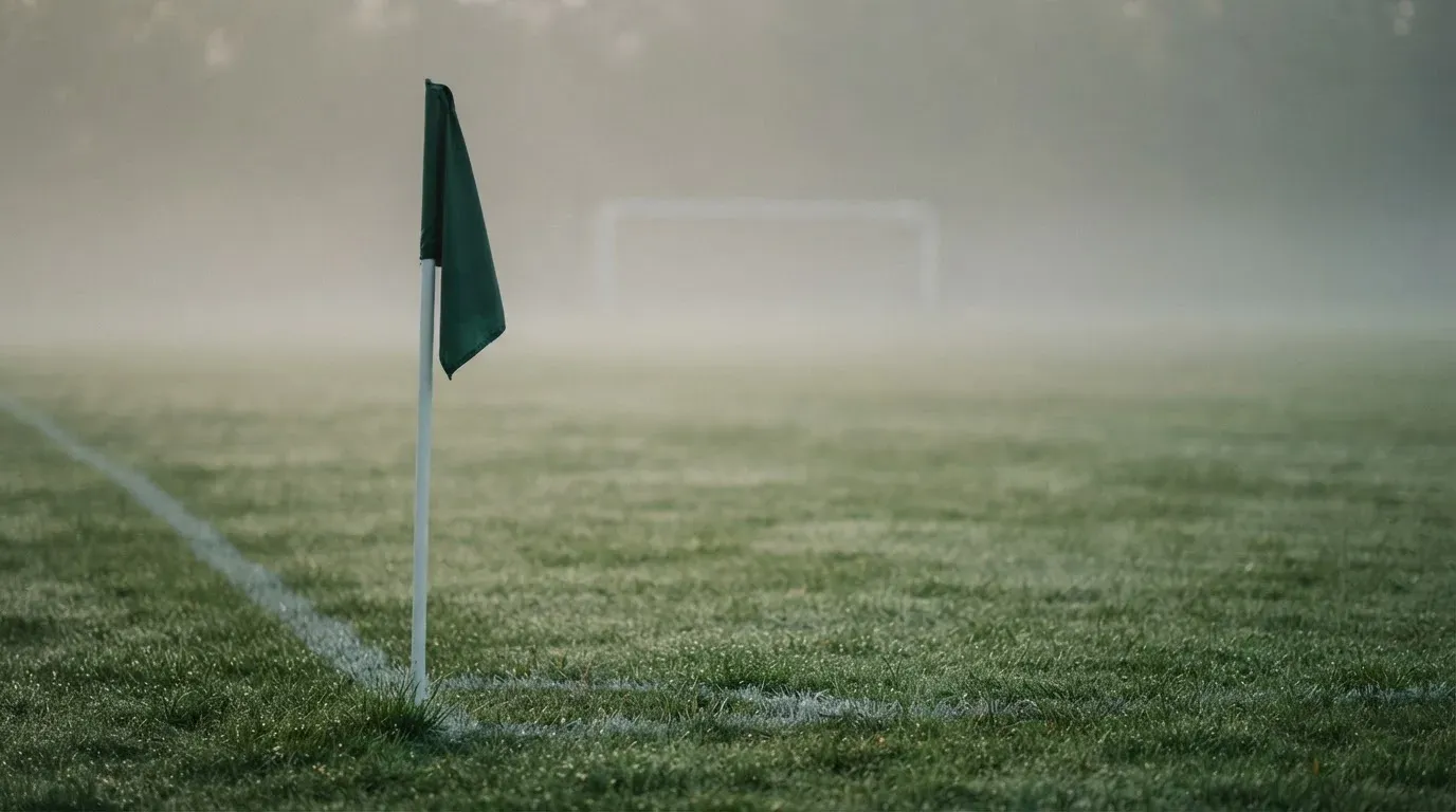 Eine Eckfahne steht am Morgen auf nassem Rasen, Tautropfen hängen im Gras und über dem Platz liegt leichter Dunst.