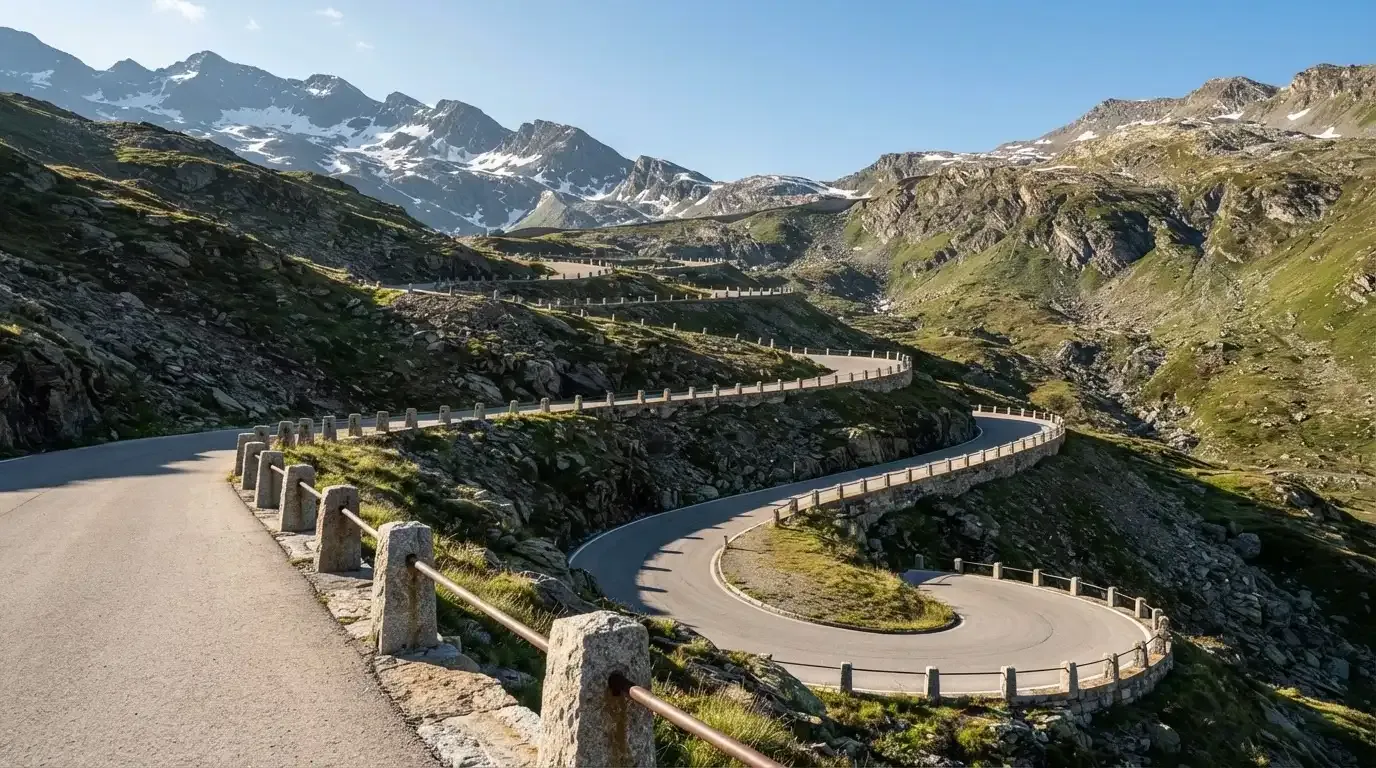 Eine leere Passstrasse mit Serpentinen windet sich im Morgenlicht einen Berg hinauf, am Rand stehen niedrige Steinpfosten.