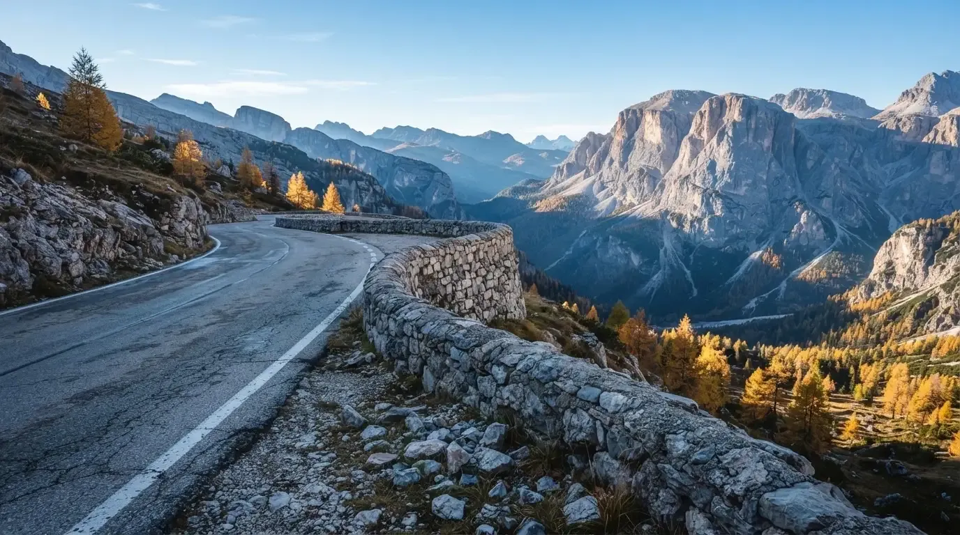 Eine Passstrasse im Hochgebirge säumt eine niedrige Steinmauer, dahinter ragen Felswände auf und der Herbsthimmel ist klar.