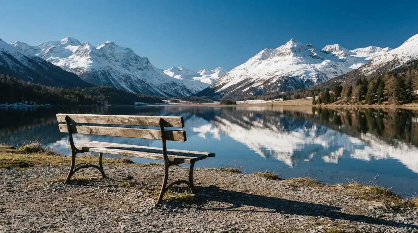 Eine Bank an einem Bergsee, dahinter schneebedeckte Gipfel im klaren Licht eines Wintermorgens.