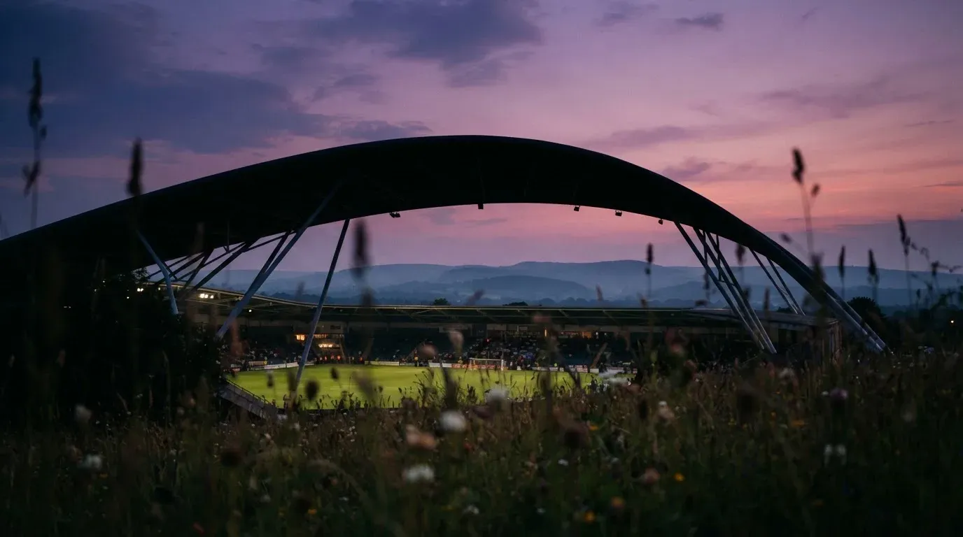 Die Silhouette eines Stadiondachs vor dem violetten Abendhimmel, dahinter eine Hügelkette.