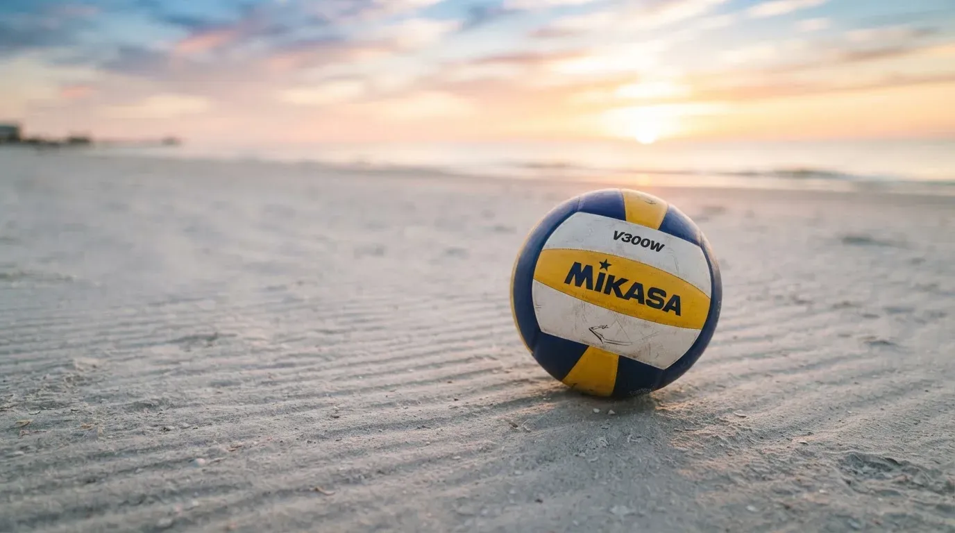 Ein Volleyball liegt auf feinem Sand an einem leeren Strand bei Sonnenaufgang.