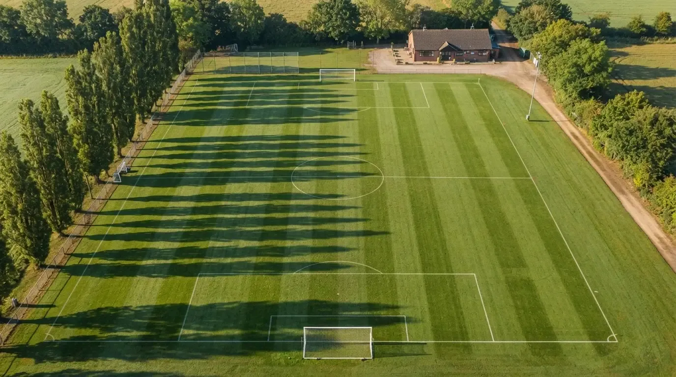Ein leerer Fussballplatz mit weissen Linien von oben gesehen im Morgenlicht, am Rand stehen zwei Tore und eine Reihe Pappeln.