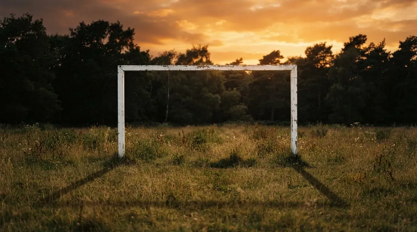 Ein Fussballtor ohne Netz steht auf einer Wiese am Waldrand, die Abenddämmerung färbt den Himmel orange.