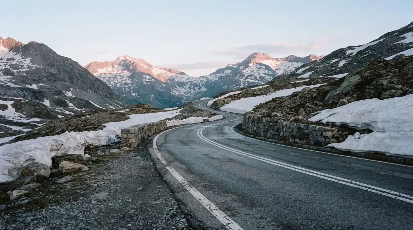 Ein Bergpass in den Schweizer Alpen mit leerer Strasse und Schneeresten am Rand im ersten Frühlicht.