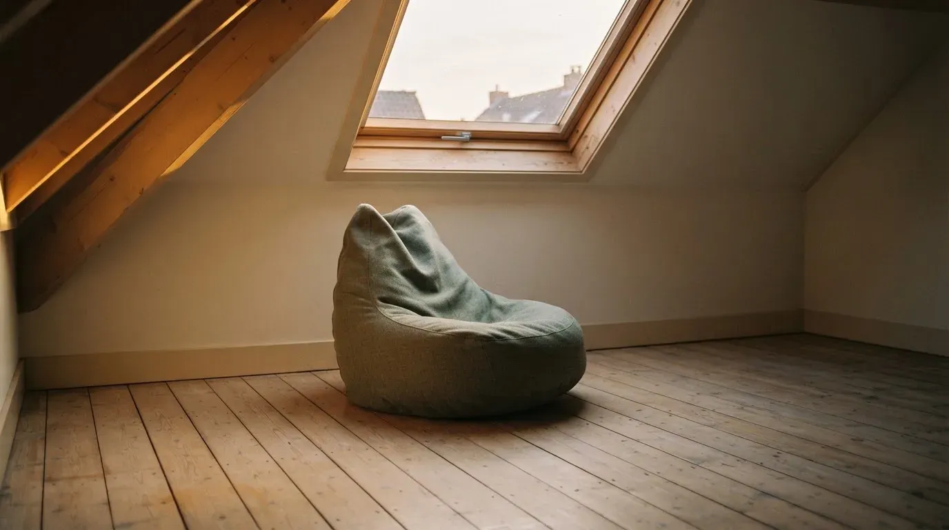 Ein leerer Sitzsack steht in einem Zimmer mit Dachfenster, Abendlicht fällt auf den Holzboden