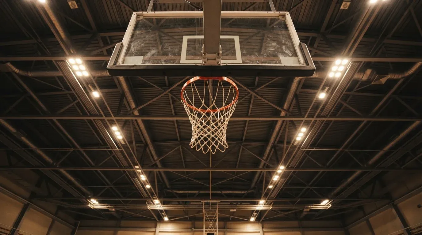 Ein Basketballkorb von unten gesehen, darüber eine Hallendecke mit Scheinwerfern und Stahlträgern.