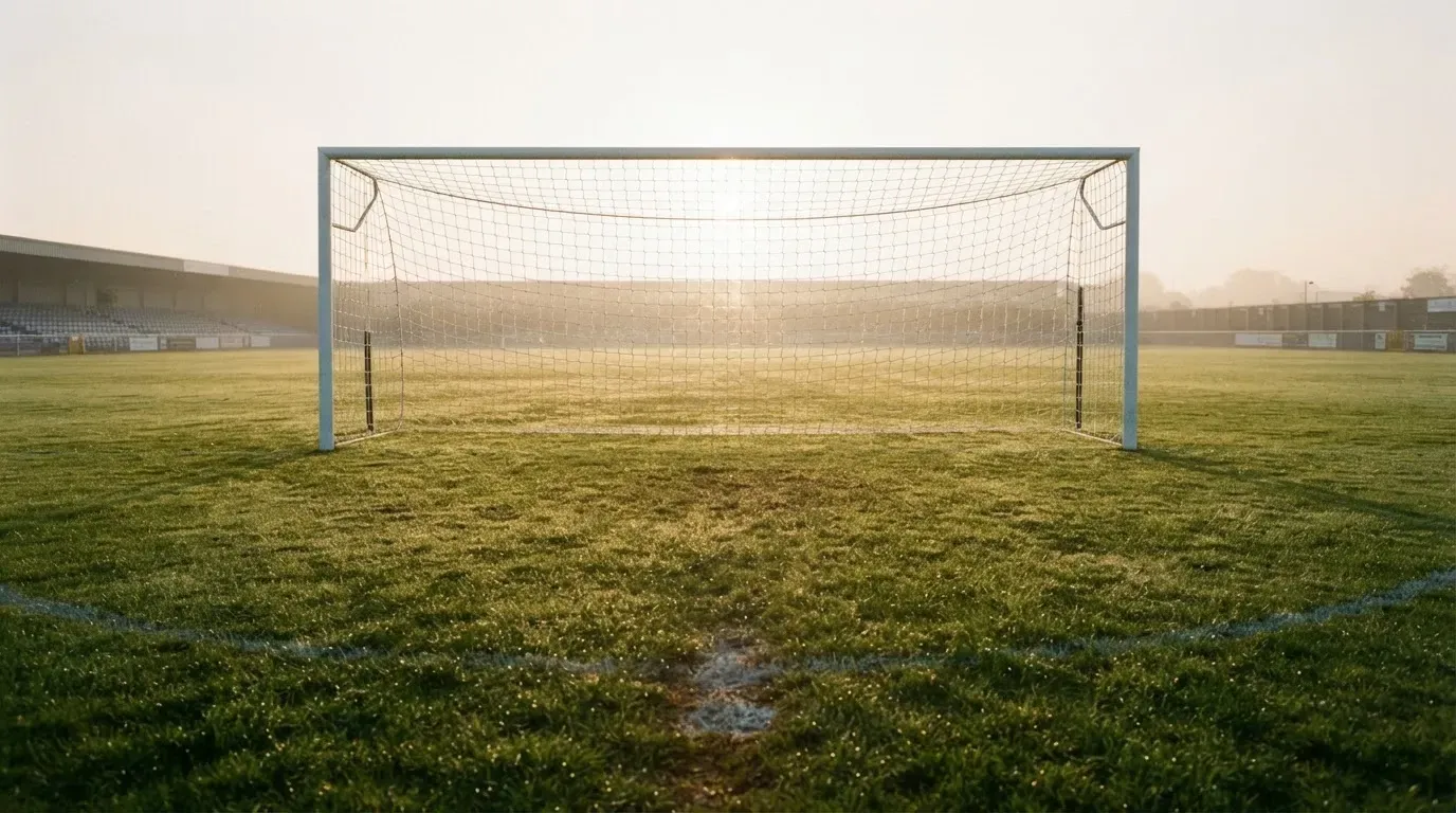 Ein Fussballtor mit Netz in der Totalen auf einem leeren Platz, Tau glänzt im Gras und die Morgensonne steht tief.