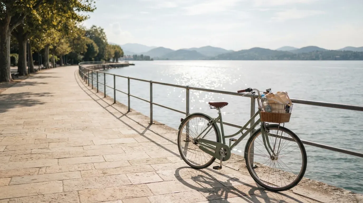 Ein Fahrrad lehnt an einem Geländer einer Uferpromenade an einem See im Sonnenlicht.