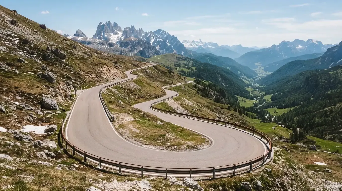 Eine Passstrasse mit Leitplanke windet sich an einem klaren Tag durch eine Berglandschaft.
