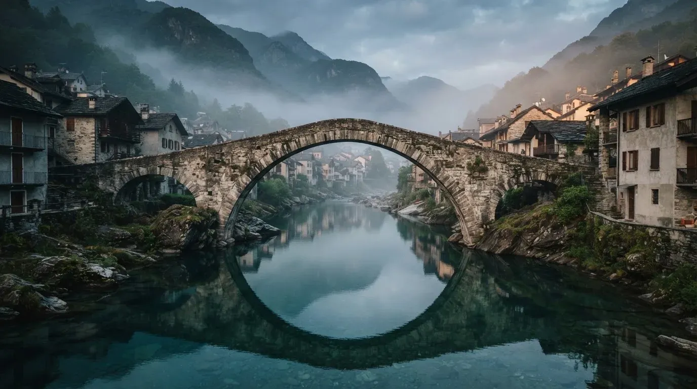 Eine steinerne Brücke über einen Fluss in einer Kleinstadt am frühen Morgen, Nebel zieht zwischen den Dächern hindurch