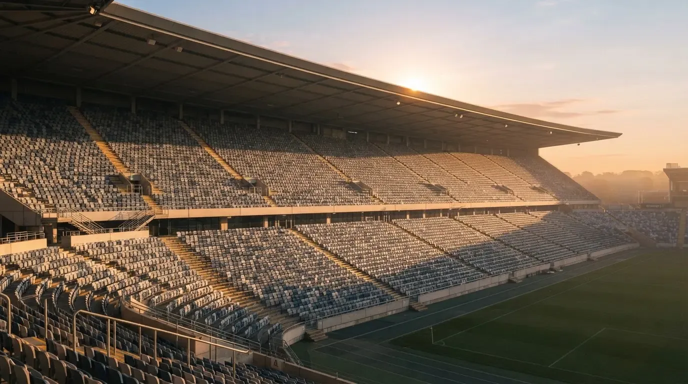 Eine leere Stadiontribüne bei Sonnenaufgang aus der Ferne, lange Schatten fallen über die Sitzreihen