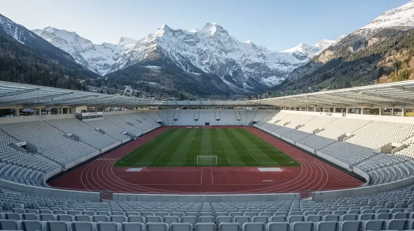 Schneebedeckte Berggipfel erheben sich im klaren Morgenlicht hinter einem leeren Stadion mit hellen Zuschauerrängen.