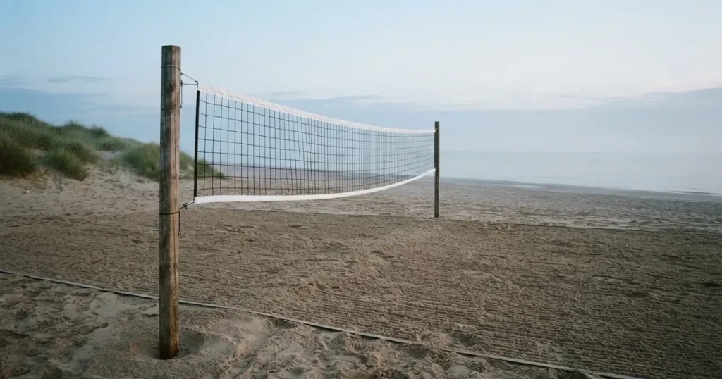 Ein Volleyballnetz spannt sich an einem leeren Sandstrand, das Meer liegt im Dunst.